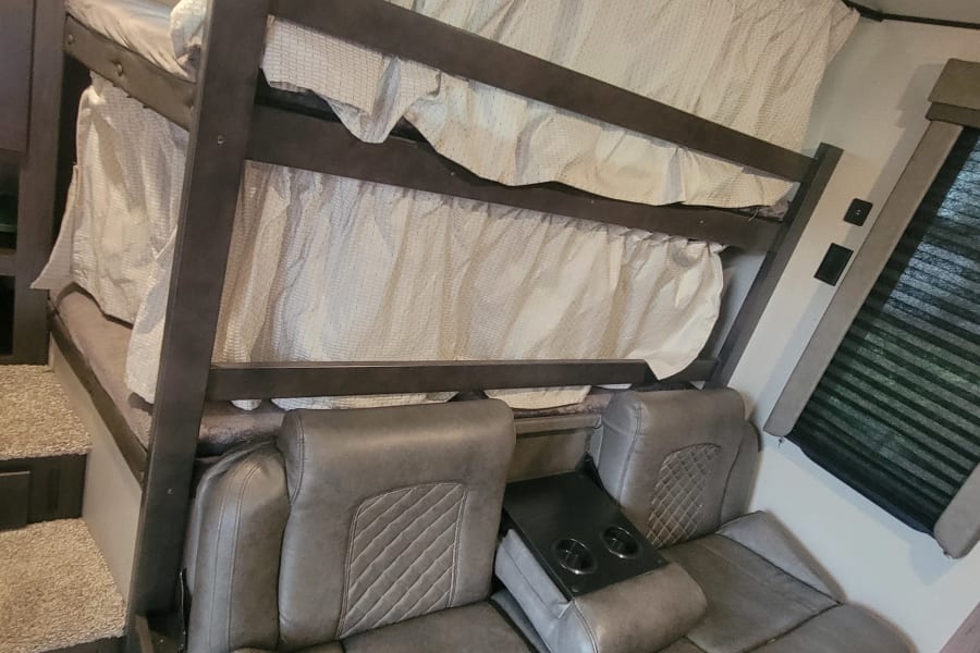 RV rental interior showing bunk beds with privacy curtains & a cozy sofa with cup holders.