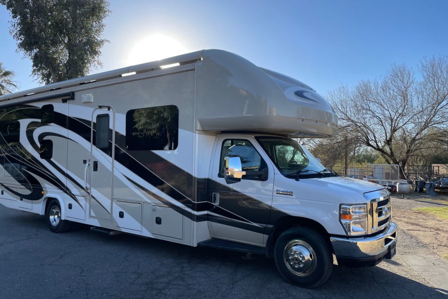 A large Class C RV rental, white with striking beige & black designs, parked on asphalt under a sunny sky.