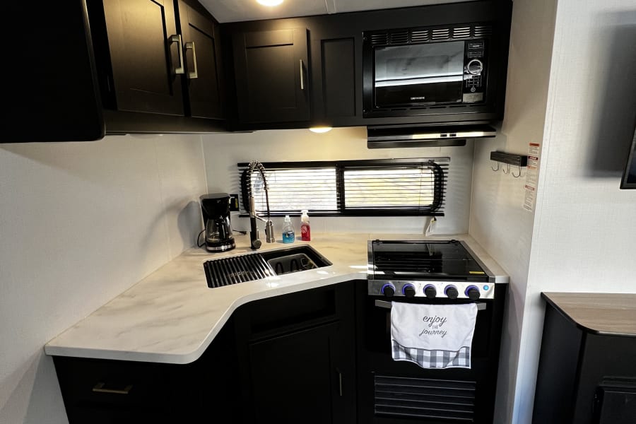 Modern RV rental kitchen with black cabinets, white counters, sink, and appliances. Ideal for your mobile adventures.