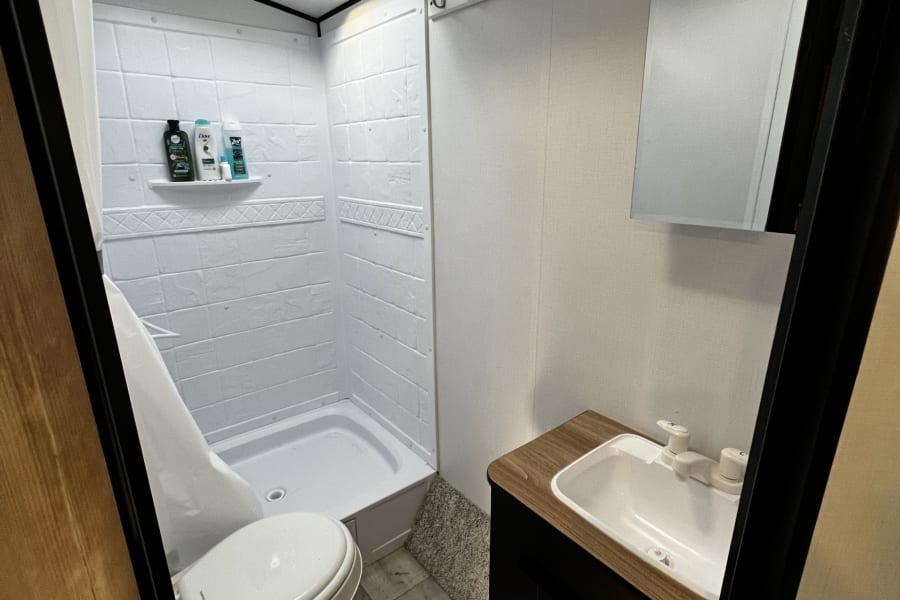 A well-lit, efficient RV rental bathroom featuring a shower, toilet, and modern sink vanity.