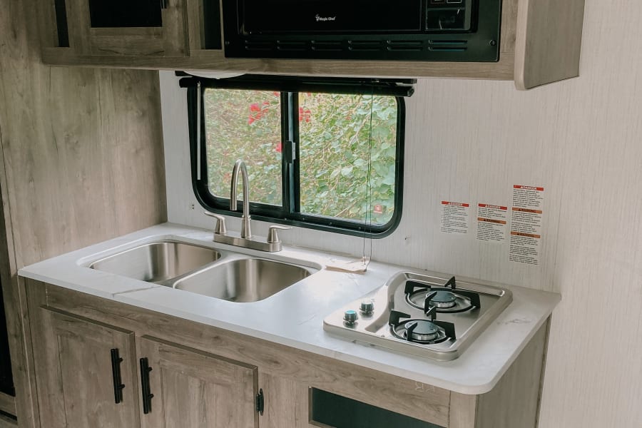 This clean RV rental kitchen features a microwave, dual sink, and two-burner stovetop, perfect for travel cooking.