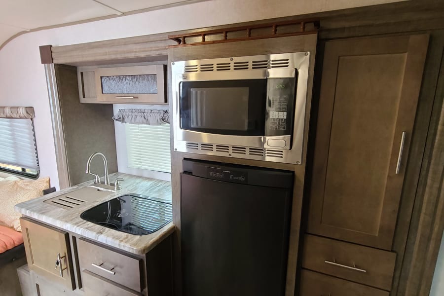 Inside a comfortable RV rental: fully equipped kitchen with sink, microwave, fridge, and cooktop, ready for your mobile home adventures.
