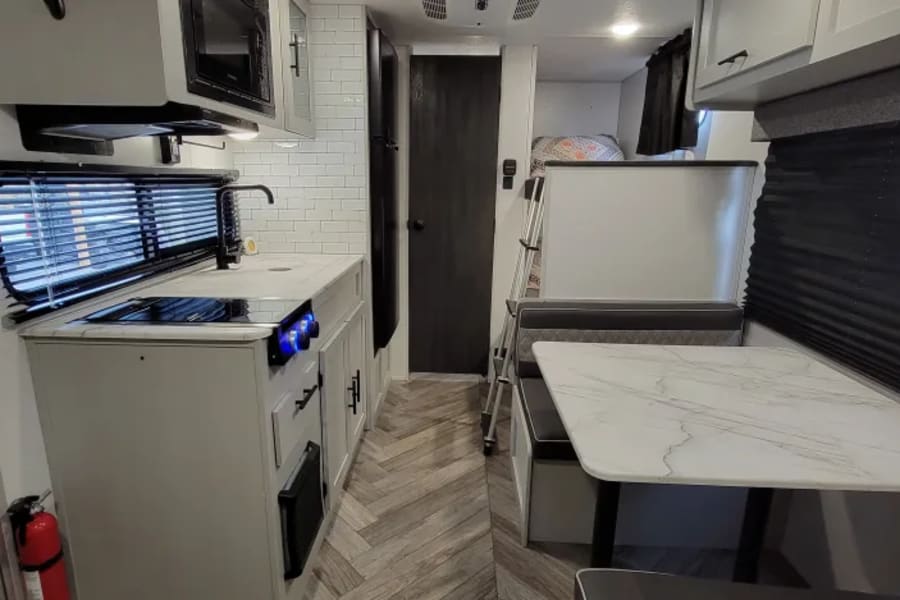 RV rental interior: kitchen with cooktop, sink, microwave, plus a dinette and bunk beds. Modern & functional for your trip.