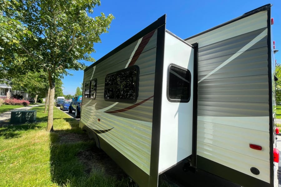 Travel trailer RV rental with slide-out extended, parked under a clear sky. Ready for your next camping adventure!