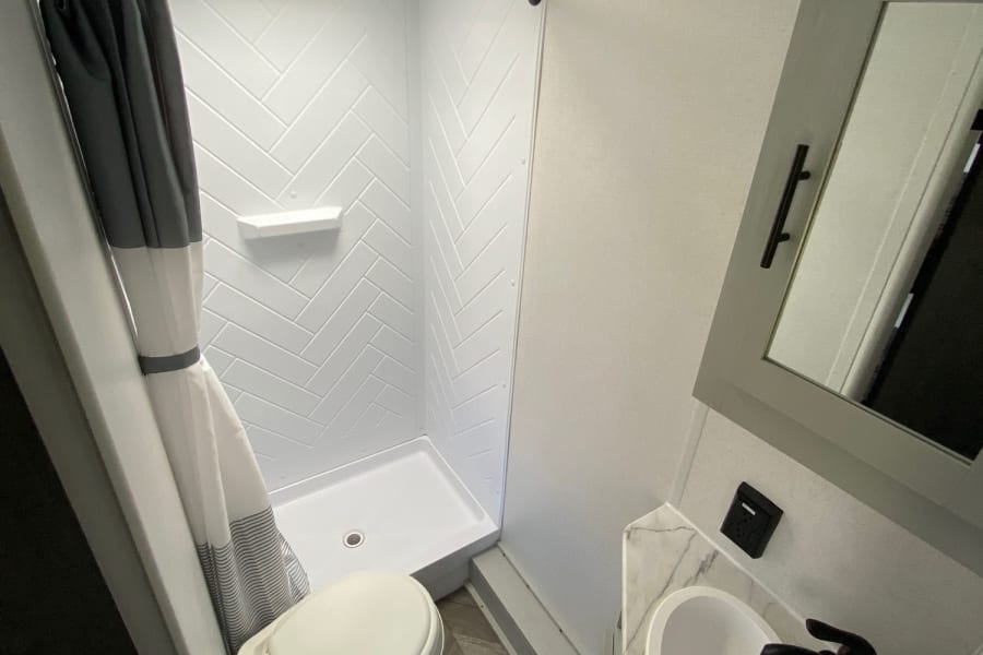 Modern RV rental bathroom features a compact shower, toilet, and vanity with sink & mirror cabinet. Bright & clean.