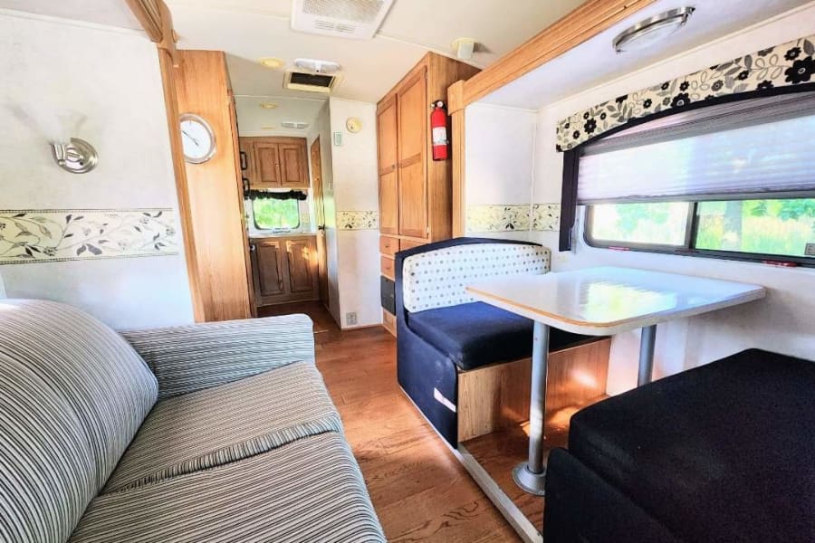 Spacious RV rental living area featuring a striped sofa, dinette with table, and wooden cabinetry. Ready for travel!