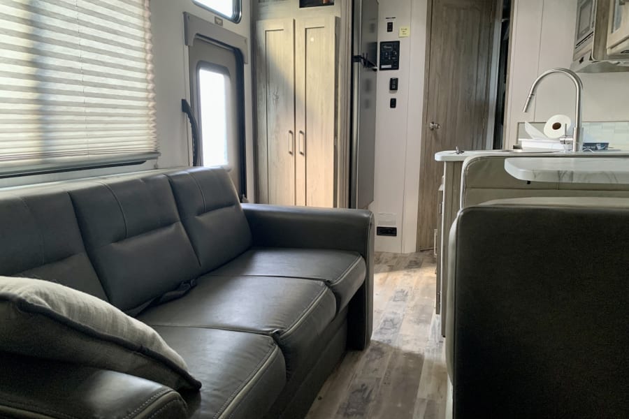RV rental interior features: a comfortable grey sofa, modern kitchen with sink, and light wood-look flooring.