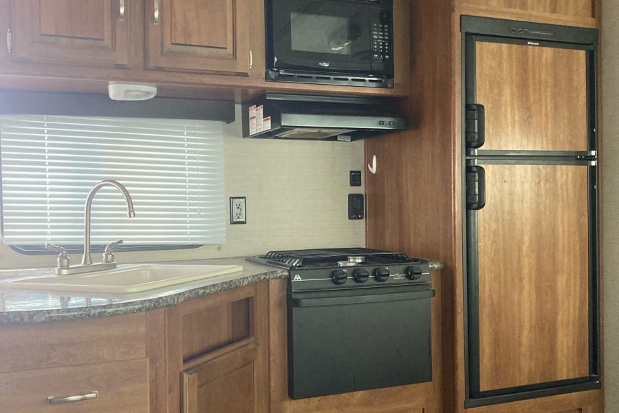 RV rental kitchen featuring wood cabinets, sink, microwave, stove, and refrigerator. Compact interior space shown.