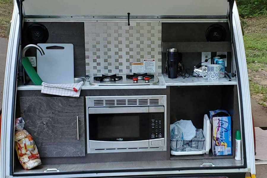 This RV rental's rear galley features a functional outdoor kitchen with sink, stove, microwave, and storage for essentials.