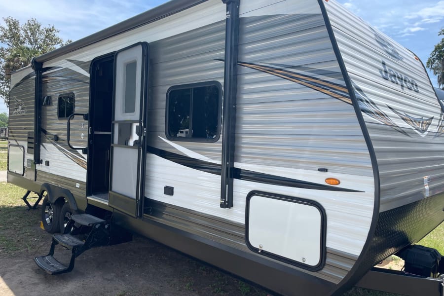 This modern Jayco Jay Flight travel trailer, with its striped grey and white exterior and open door, is ready for an RV rental adventure.
