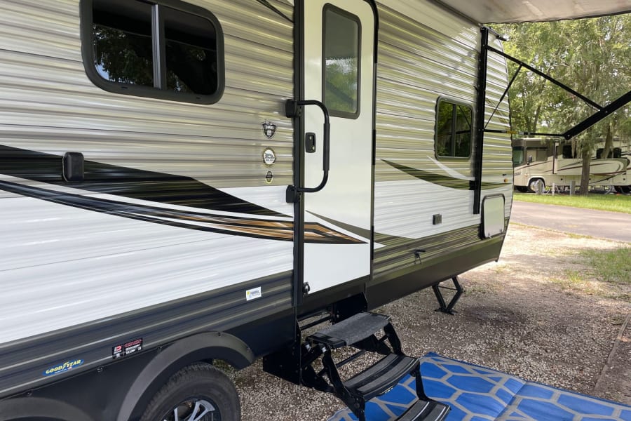Detailed view of an RV rental: a travel trailer at a campsite, showing its door, steps, and extended awning.
