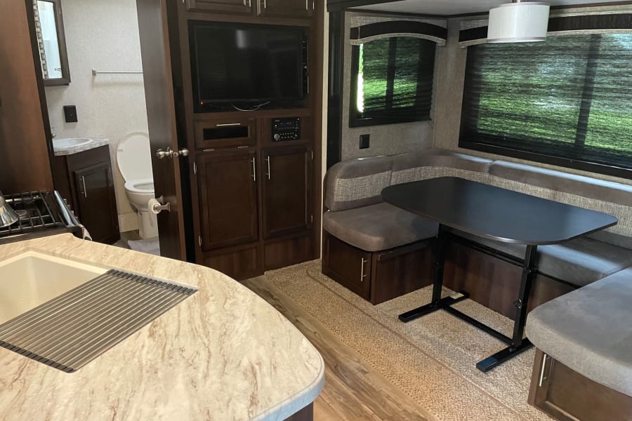 Experience comfort in this RV rental! View of the kitchen, entertainment center, dinette, and bathroom.
