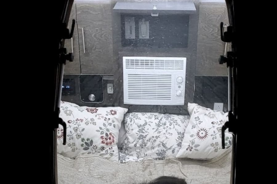 Inside a comfy RV rental: bed with patterned pillows, AC unit, and a black cat napping.