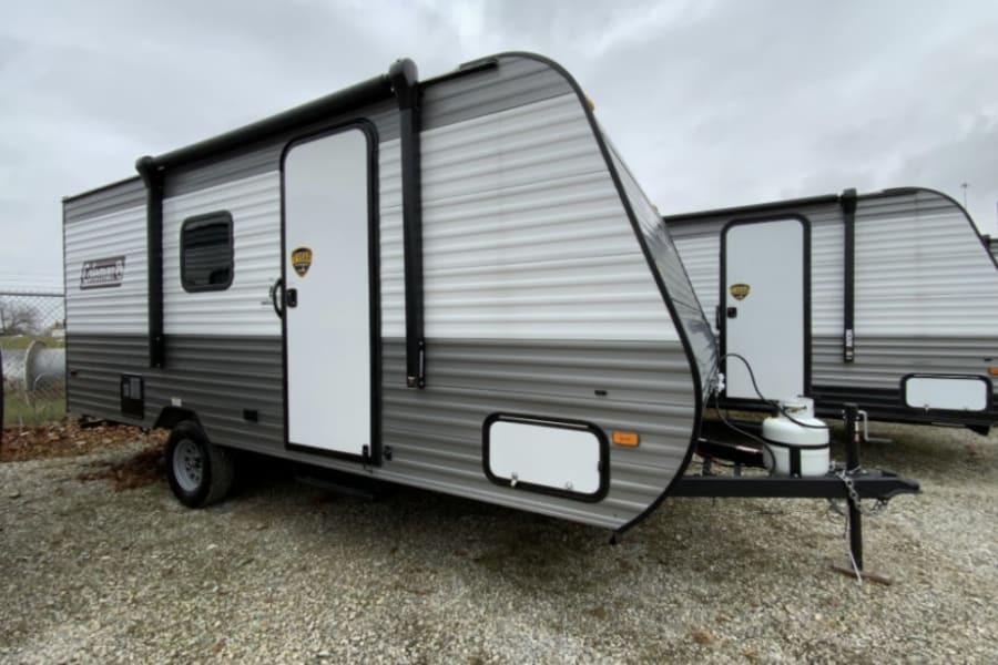 Explore adventure with this RV rental: a new gray and white travel trailer, equipped with an awning and propane tank.
