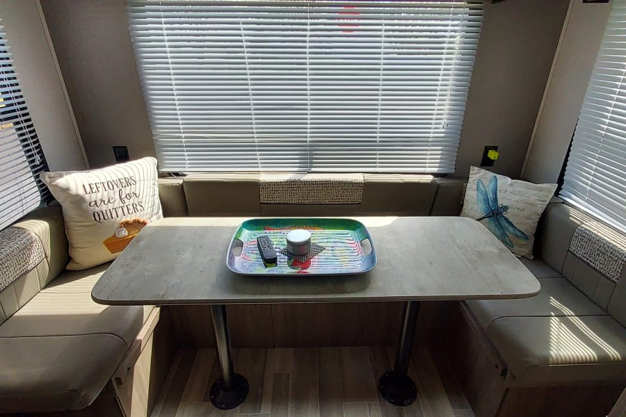 Bright RV rental interior: dinette, ample cabinets, blinds, and wood-look flooring. Cozy travel home.