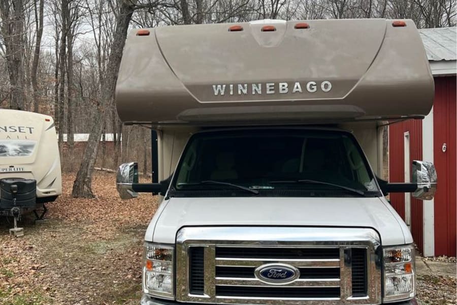 White Ford Winnebago Class C motorhome, great for an RV rental. Parked in a wooded area.