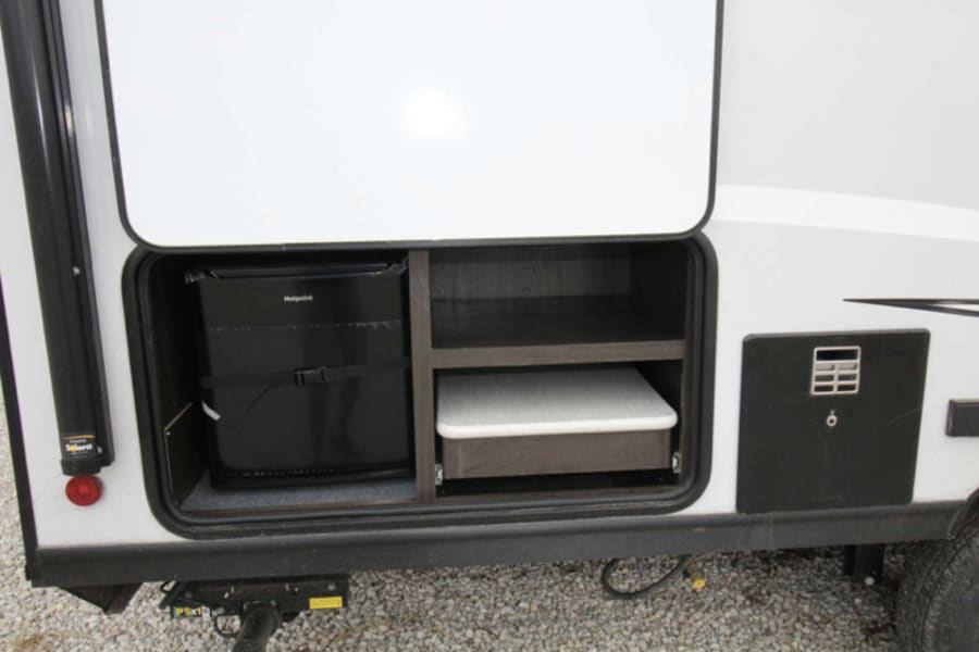 Explore this RV rental's outdoor kitchen: a Hotpoint mini-fridge, pull-out counter, and storage for convenient camping.