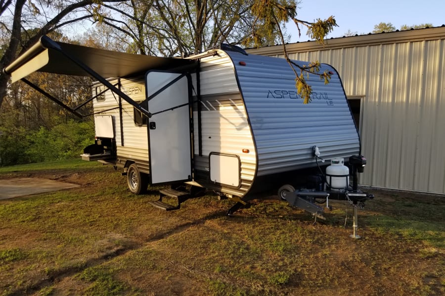 This silver travel trailer RV rental, with awning extended and outdoor kitchen open, sits ready in a grassy outdoor setting.