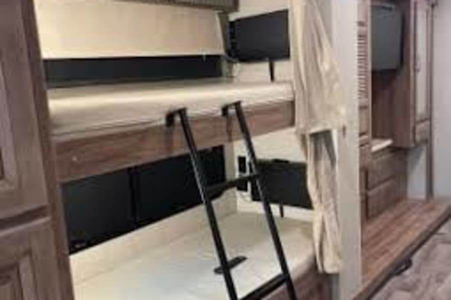 Cozy RV rental bunk beds: comfortable interior sleeping area for travel, complete with ladder and TV for your next adventure.