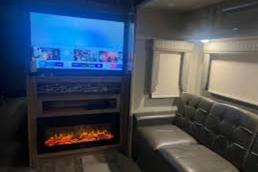 Cozy RV rental living area with a large TV, glowing electric fireplace, and dark sofa. Perfect for relaxing nights on the road.