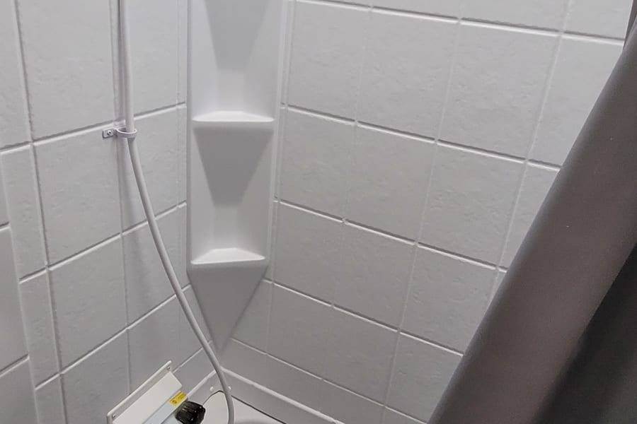 This RV rental offers a clean, compact white shower stall, complete with built-in shelves and a handheld showerhead.