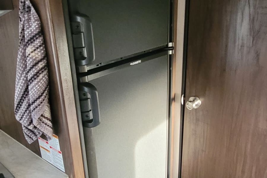 Built-in Dometic refrigerator in an RV rental, with the wooden lid open revealing the interior. Ideal for road trips.