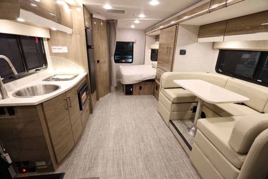 Explore this RV rental's inviting interior: compact kitchenette, U-shaped dinette, and rear bedroom.