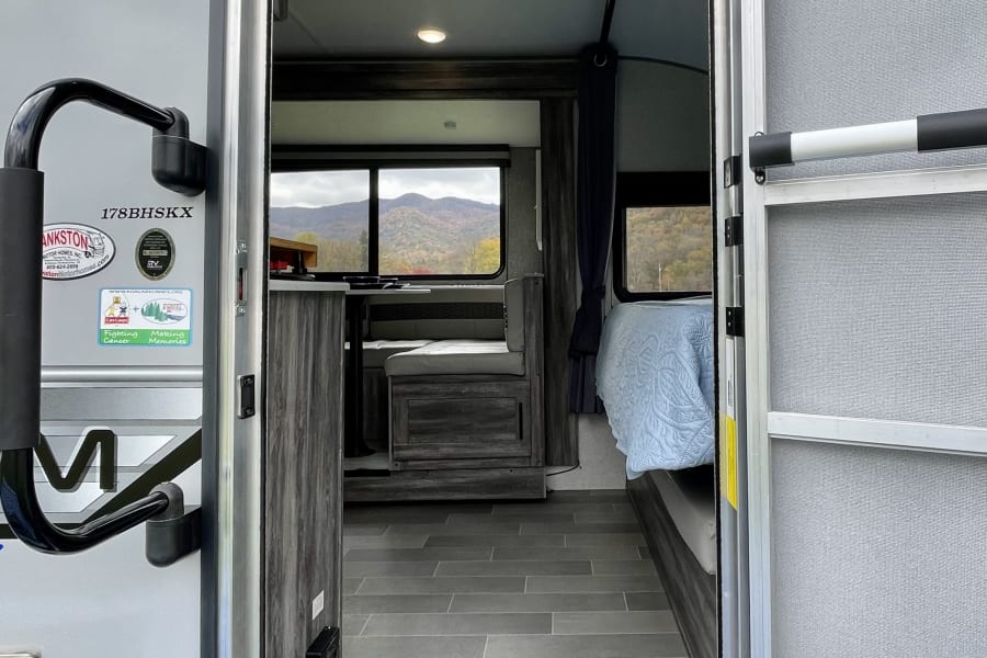 View from an open RV rental doorway, showcasing a compact interior with dinette, bed, and scenic mountain views outside.