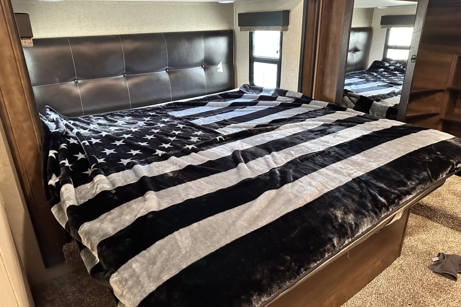 Cozy RV rental bedroom featuring a large bed with a black & white flag blanket & dark headboard.