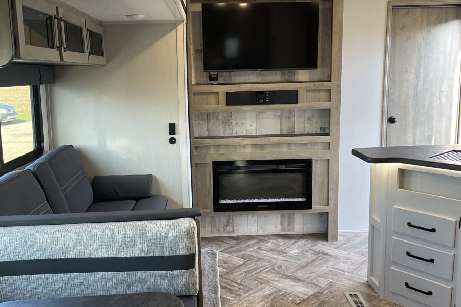 Spacious RV rental interior featuring a cozy living space, modern entertainment center with fireplace, and functional kitchen area.