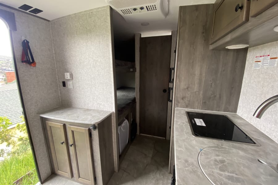 RV rental interior: A compact kitchen with stove and sink, bunk beds, and AC unit create a comfy mobile home.