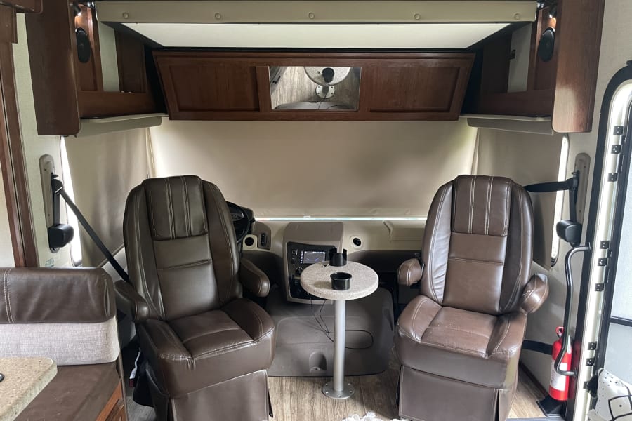 RV rental's front cabin with brown captain's chairs, a dashboard, small round table, and a fire extinguisher near the door.