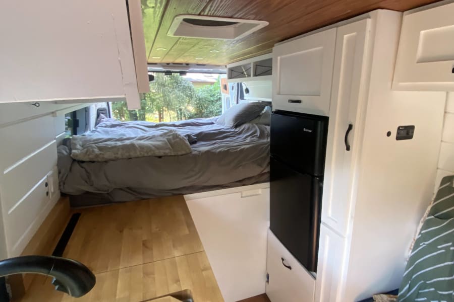 RV rental interior featuring a compact kitchen with fridge, comfy bed, and ample storage within a modern camper van.
