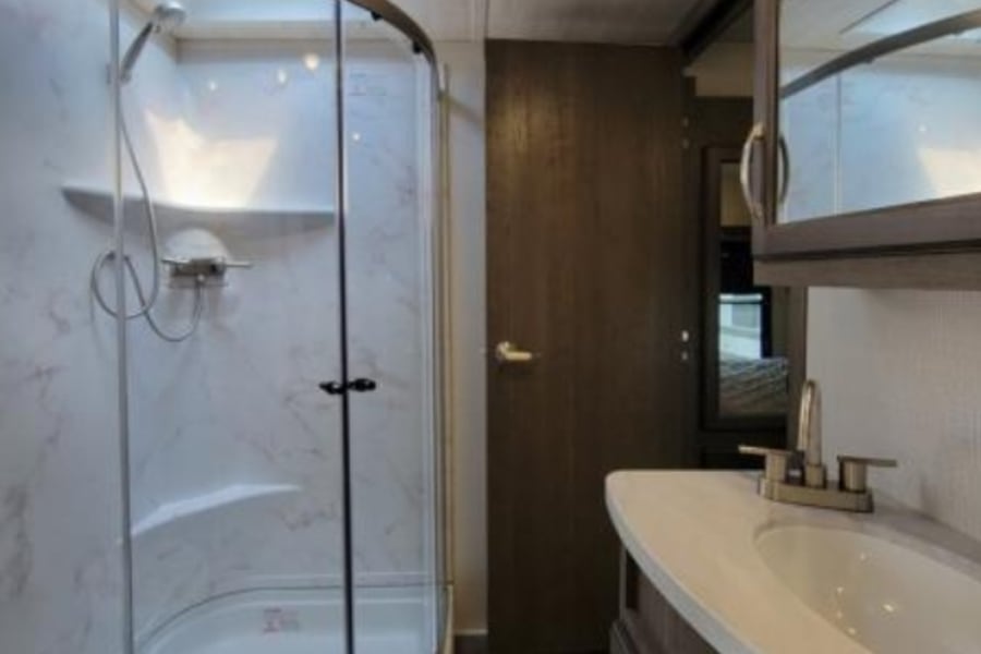 Modern RV rental bathroom with a glass corner shower, vanity, sink, and toilet. Clean and compact for travel comfort.
