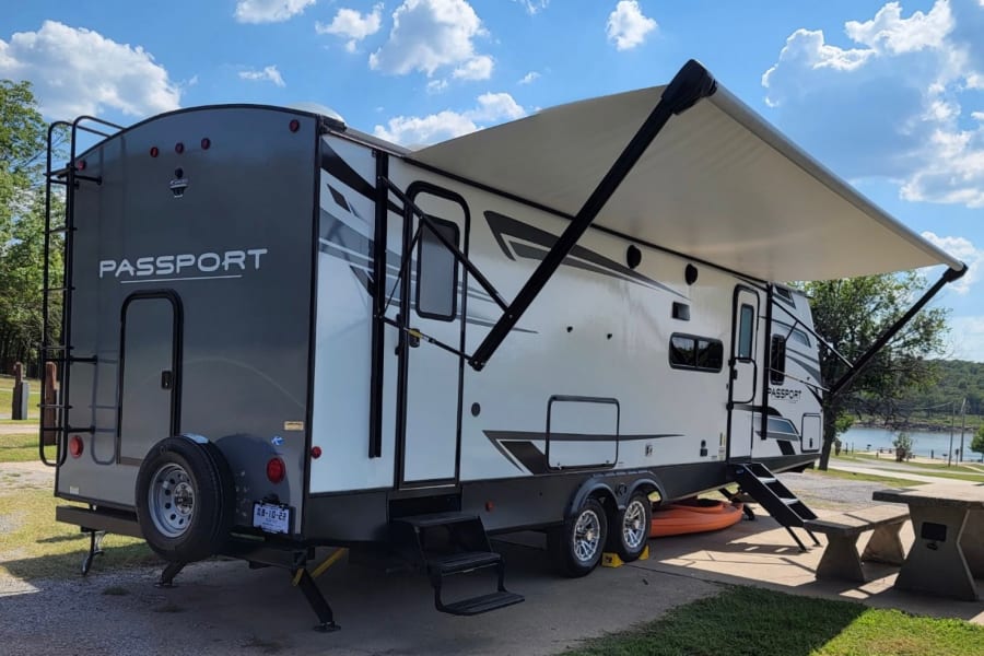 This Passport RV rental rests lakeside, awning out, at a peaceful campsite.