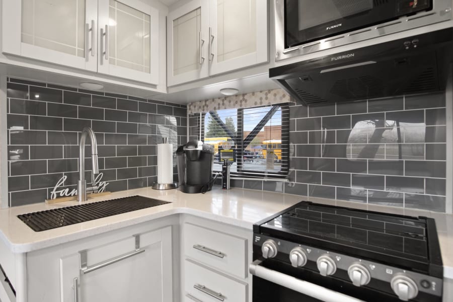Tour this RV rental's sleek kitchen! It boasts a stove, microwave, Keurig, and chic grey tile backsplash.