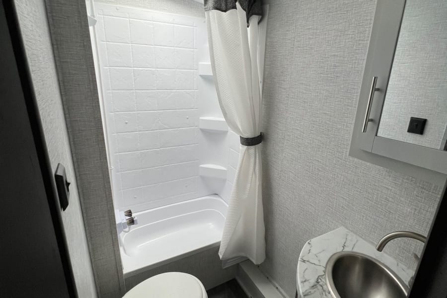 Step inside this modern RV rental bathroom, featuring a bright shower/tub, toilet, sink, and stylish gray walls.