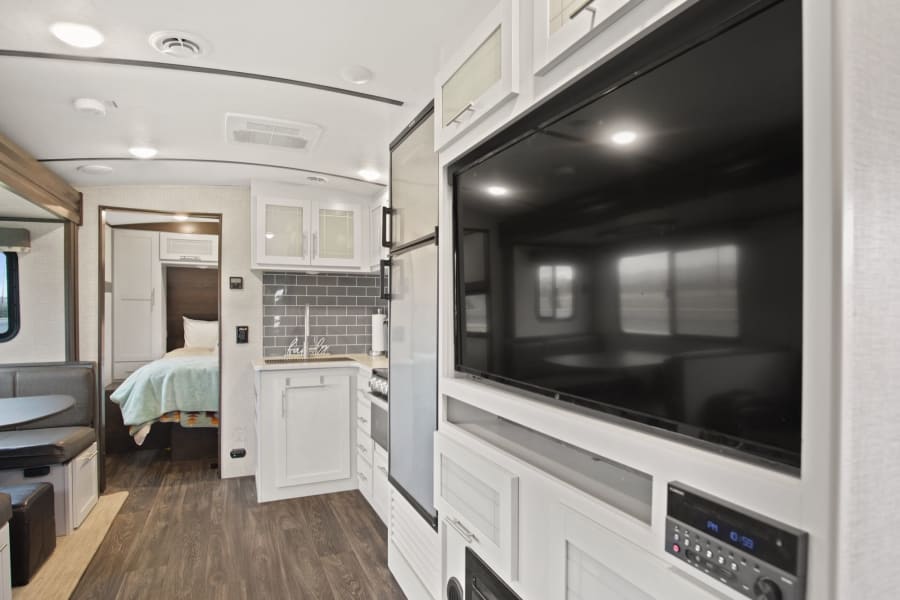 Experience comfort in this modern RV rental interior, featuring a bright kitchen, dinette, bedroom, and living area with a TV.