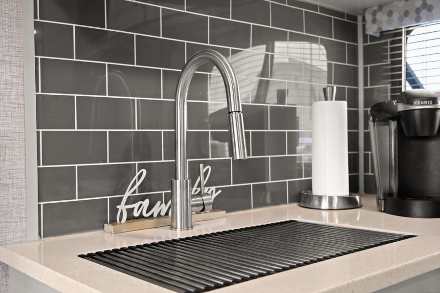 Enjoy this RV rental's modern kitchen: gray subway tile, chrome faucet, roll-up drying rack, & Keurig coffee maker.