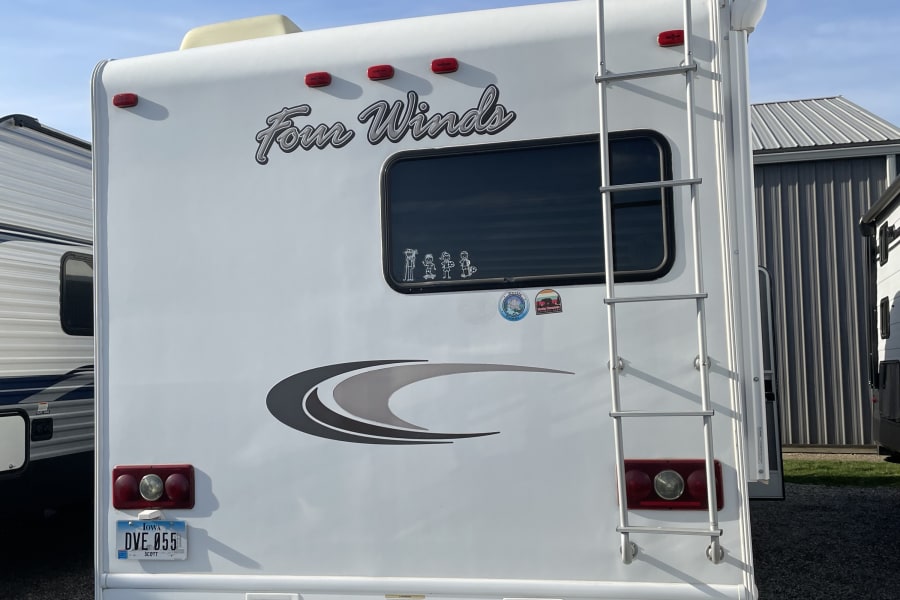 The back of a white Four Winds RV rental with a ladder, window decals, and Iowa license plate.