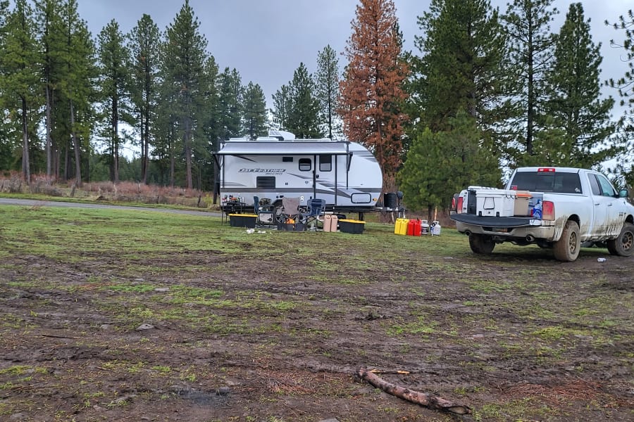 RV rental and pickup truck parked at a muddy campsite, surrounded by evergreen trees.