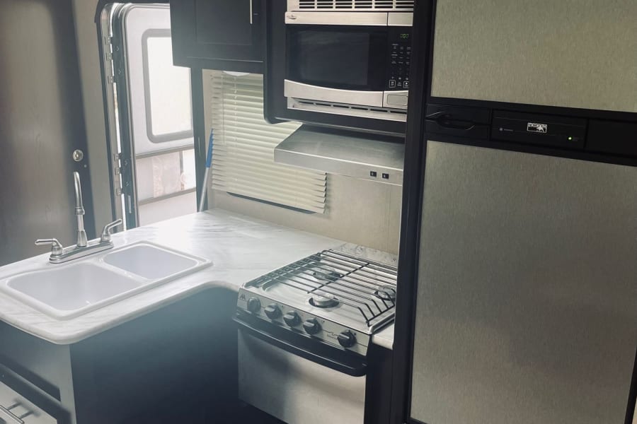RV rental kitchen: Features a double sink, gas stove, microwave, and refrigerator, all within a modern, dark-themed interior.