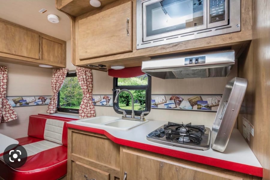 Retro-style rv rental interior with red dinette & fully equipped kitchen, including microwave & stove for your travels.