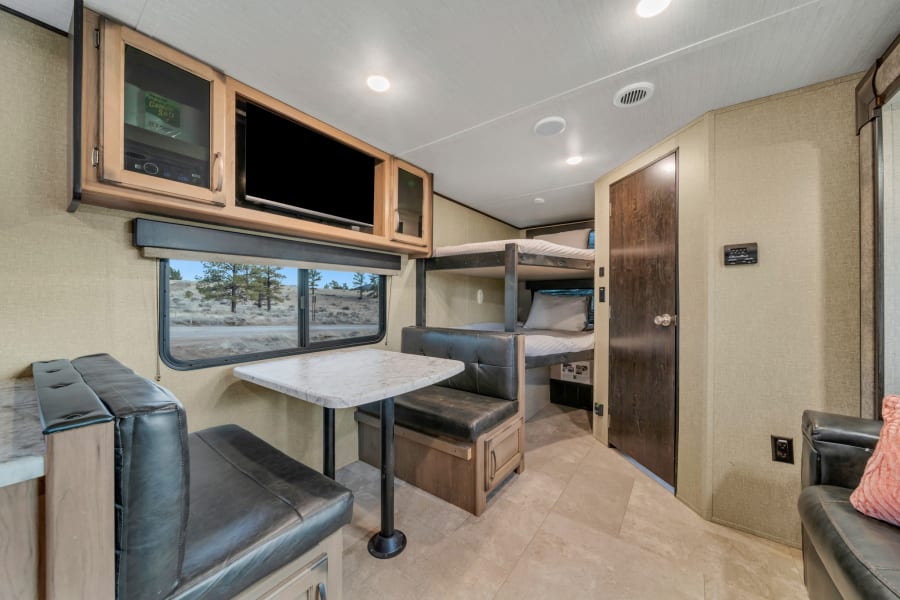 RV rental interior: dinette, bunk beds, TV, and a scenic window view. Comfortable and ready for travel adventures.
