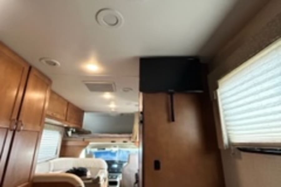 Inside this **RV rental**, find a compact living space: a cozy bed, wall-mounted TV, and wood cabinets. Perfect for road trips!