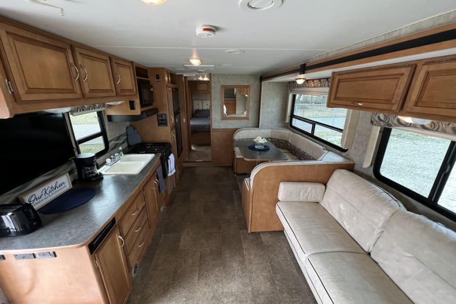 Inside this rv rental: a functional kitchen, dining area, comfortable sofa, and a peek into the cozy bedroom.