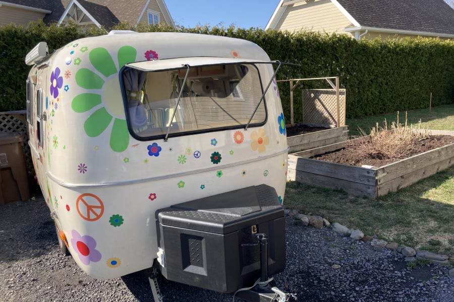 Unique, flower-power rv rental: a retro travel trailer with peace signs and colorful decals, parked outdoors on gravel.