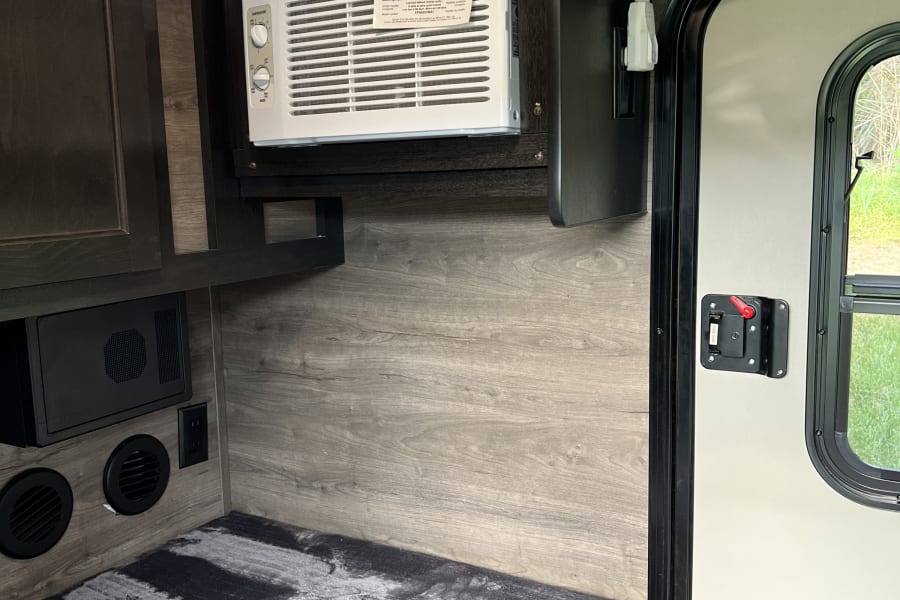 Inside an RV rental: a compact living space featuring a wall-mounted AC, comfortable bedding, and practical cabinetry.