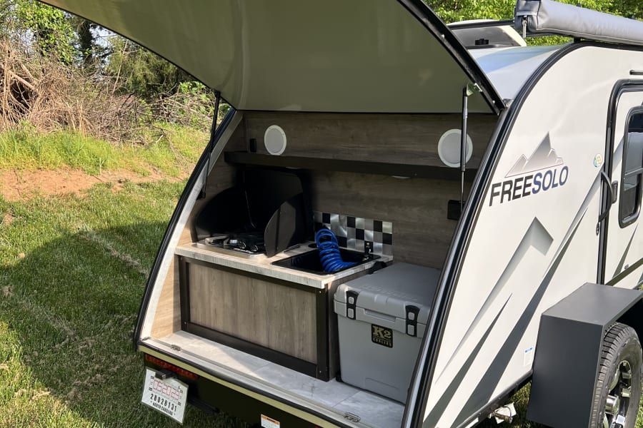 RV rental: A teardrop camper with its rear outdoor kitchen open, revealing a stove, sink, and cooler, set for camping.