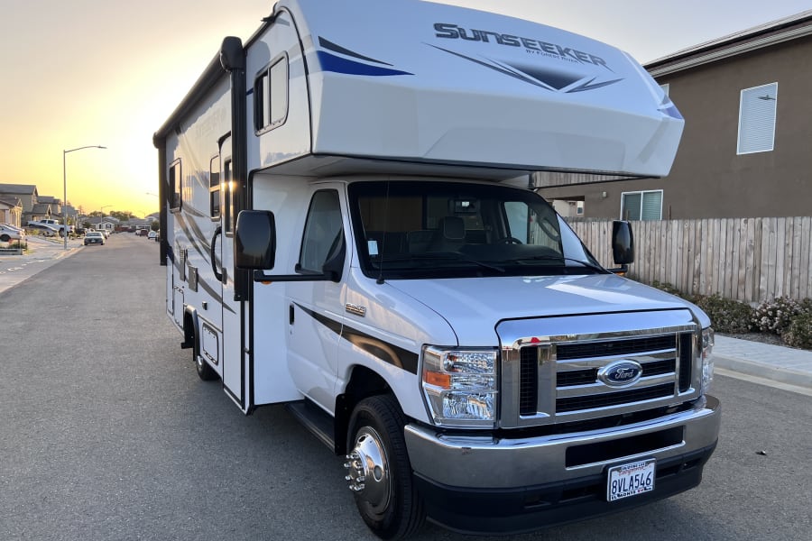 White Sunseeker RV rental parked on a quiet residential street, bathed in the glow of sunset.